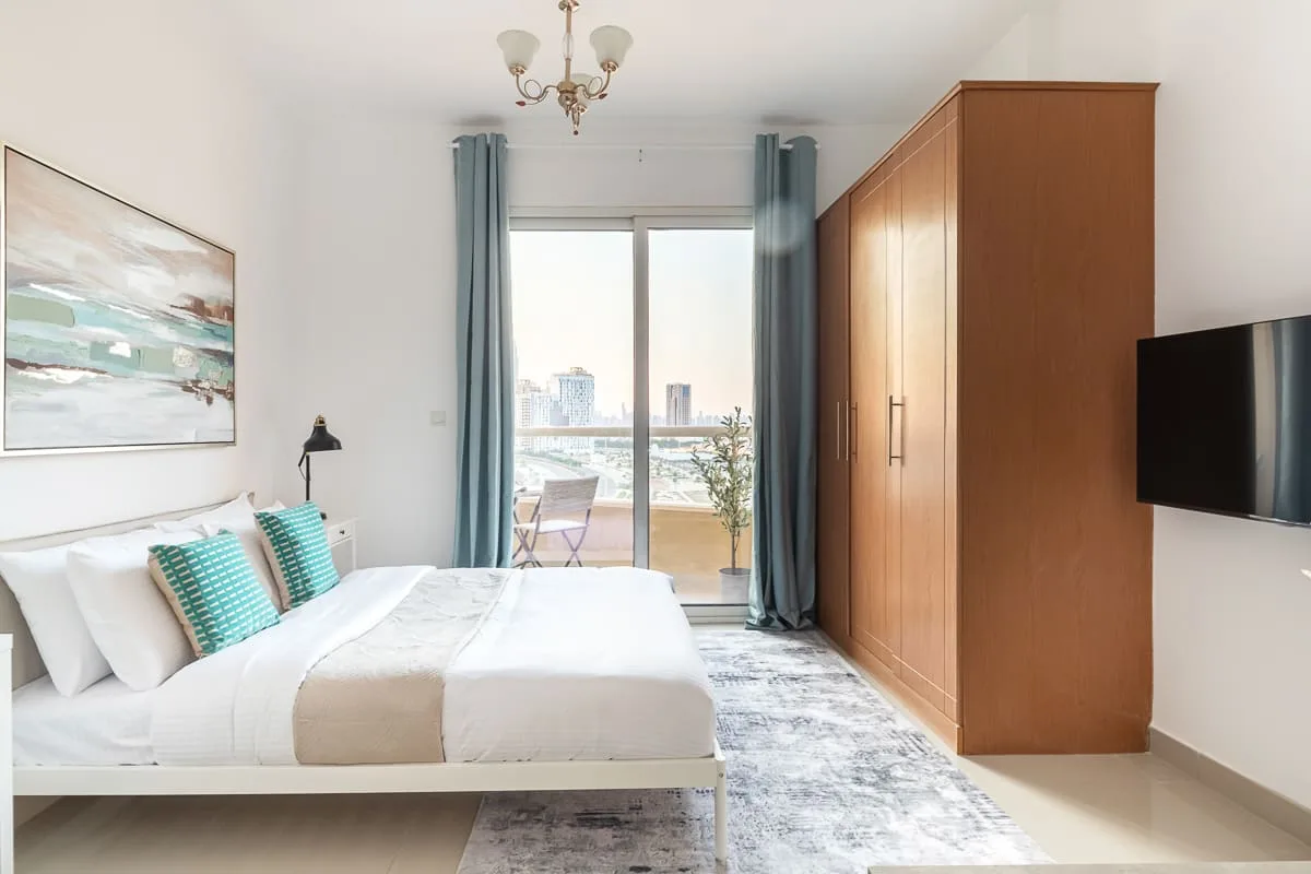 A bright bedroom with a bed, wardrobe, and glass doors opening onto a balcony.