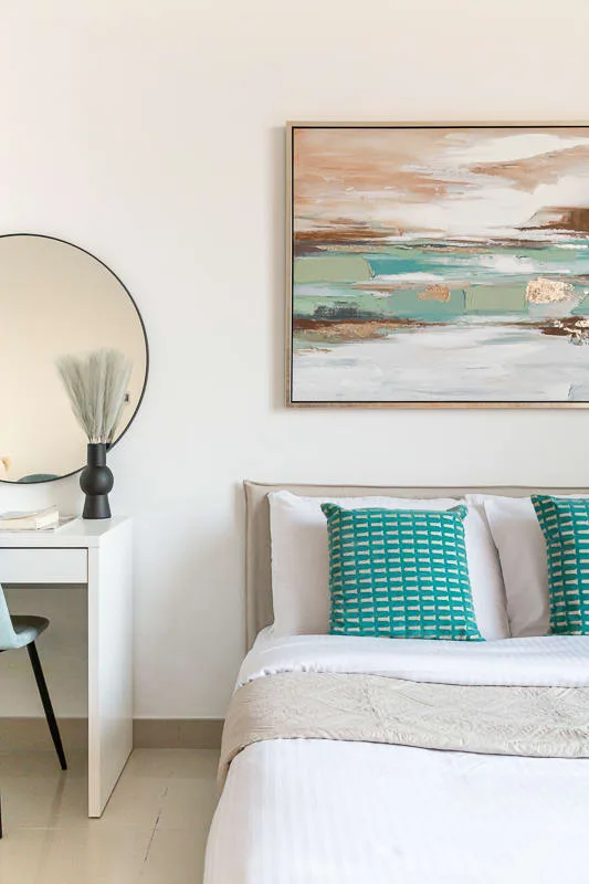 Bedroom with a bed, teal cushions, and framed abstract artwork.
