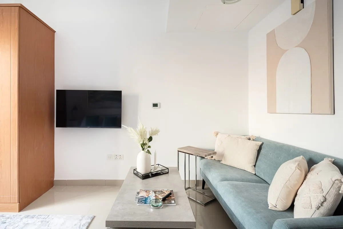A living room with a blue sofa, coffee table, and wall-mounted television.