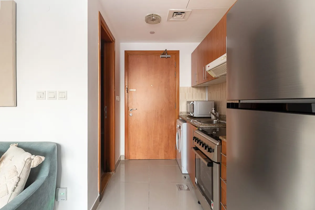 A compact kitchen with wooden cabinets and stainless steel appliances beside a hallway.