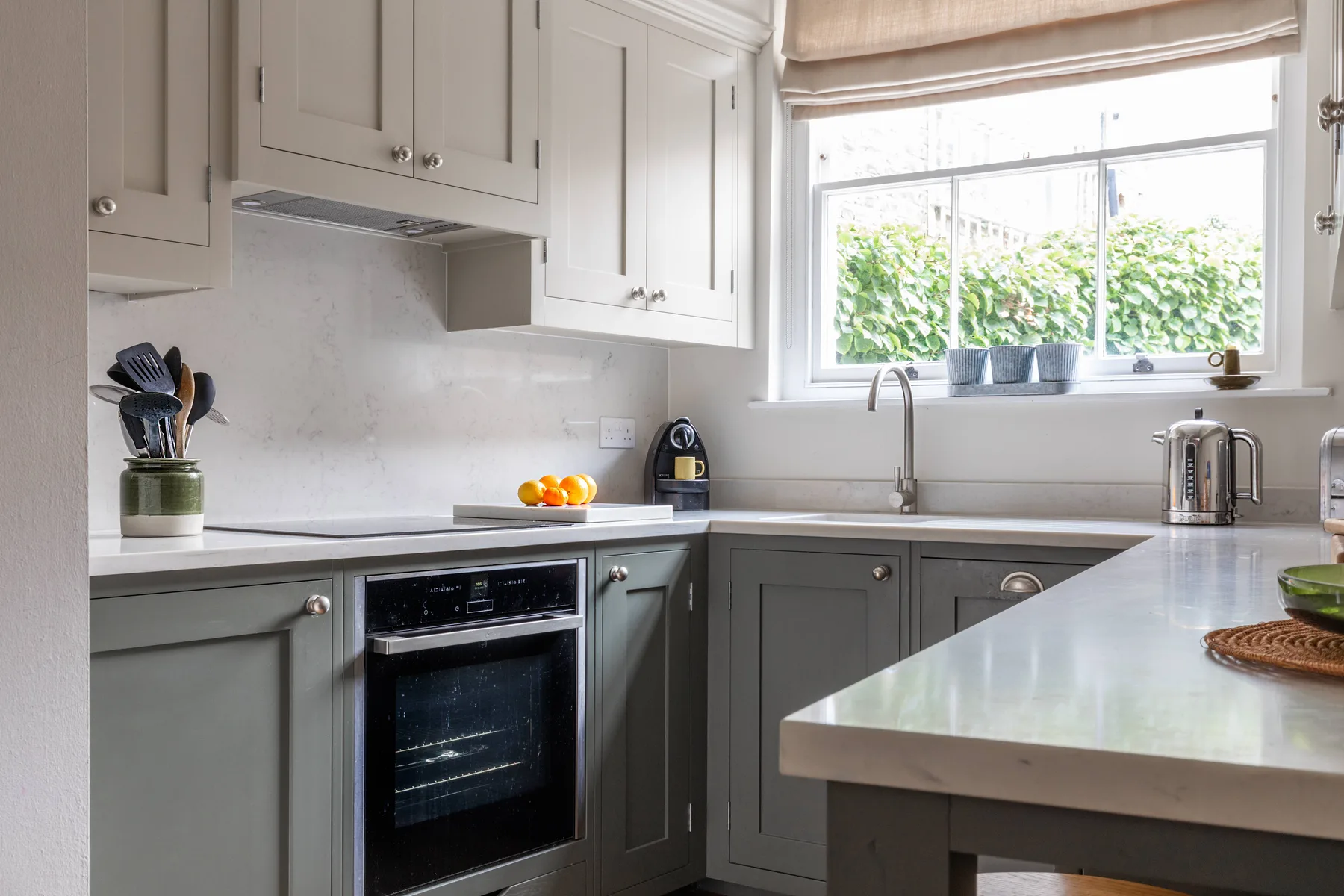A bright kitchen with gray cabinets, pale countertops, and a large window.