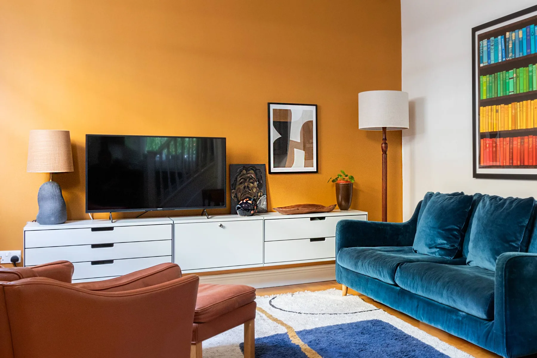 A living room with a television, blue seating, and an orange accent wall.