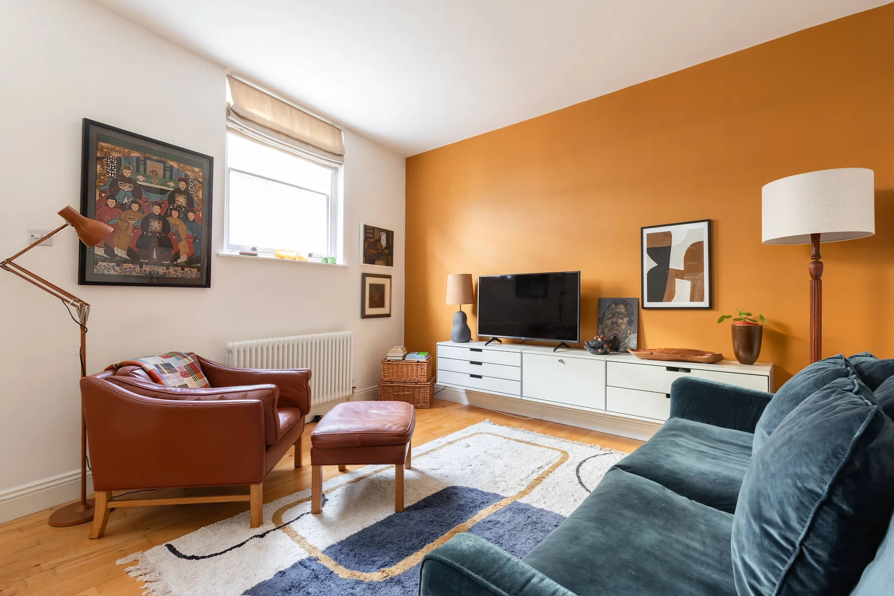 A living room with seating, a television, and artwork against an orange wall.