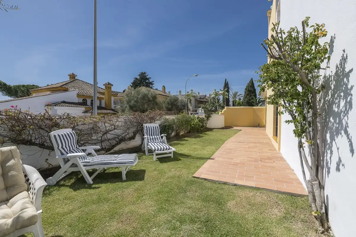 A small garden with lawn, outdoor seating, and a paved path beside the building.