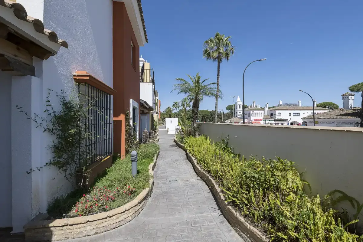 A paved walkway runs between planted garden beds beside the buildings.
