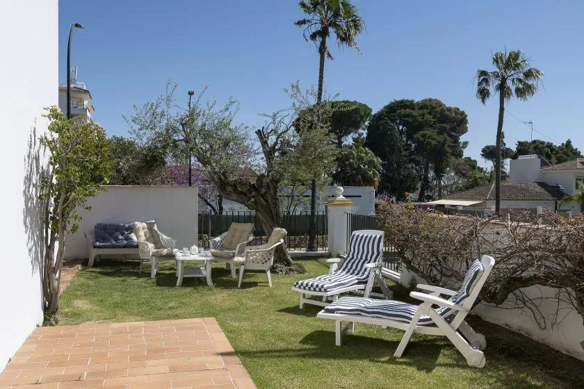A garden seating area with white lounge chairs beside a tiled patio.