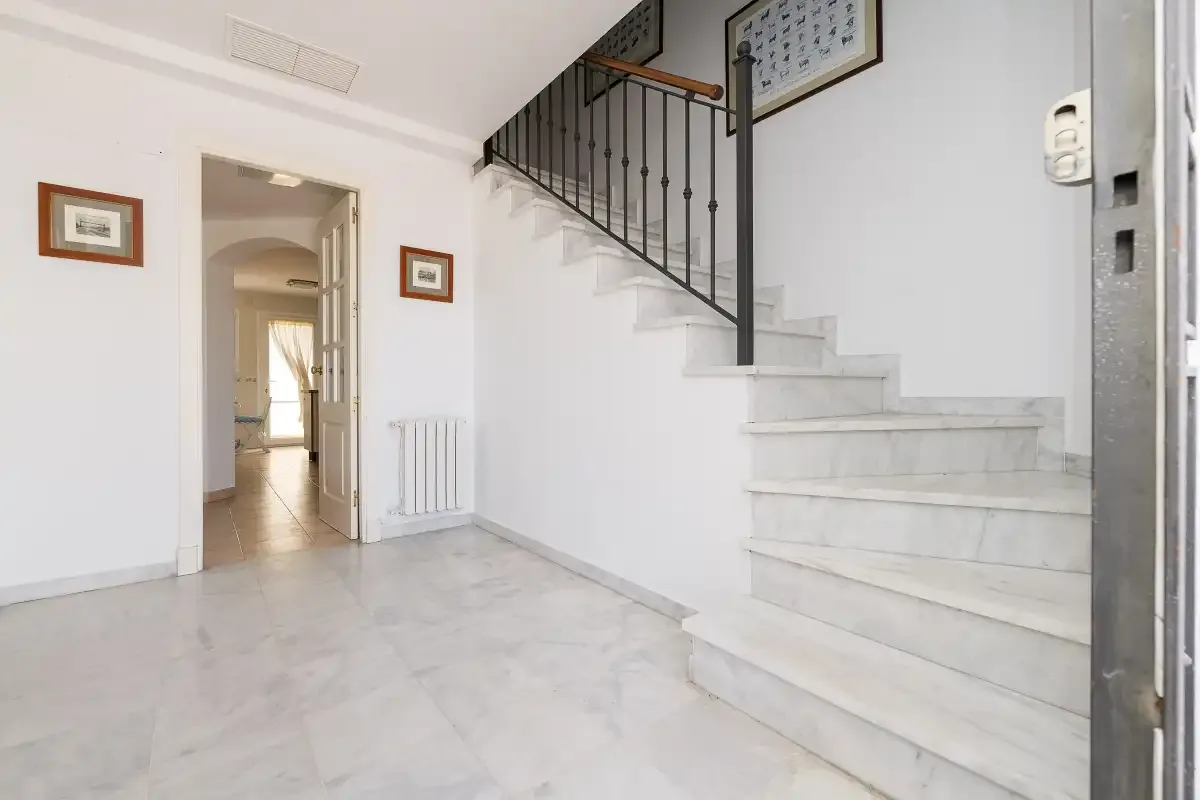 A bright interior entry hall with a staircase and an open doorway.