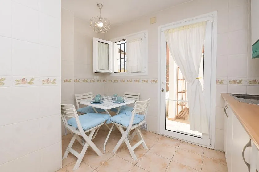 A small dining area with a table and blue-cushioned seating beside a curtained glass door.