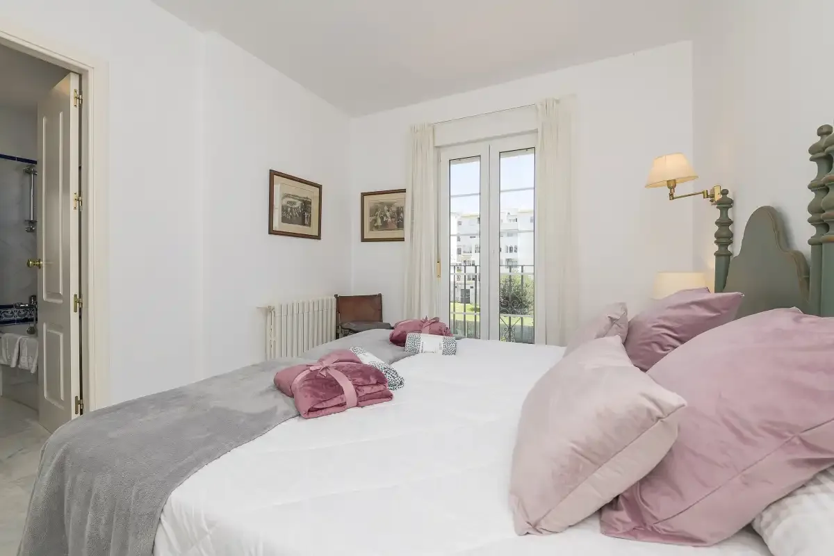 A bedroom with a large bed, pale bedding, and French doors opening to a balcony.