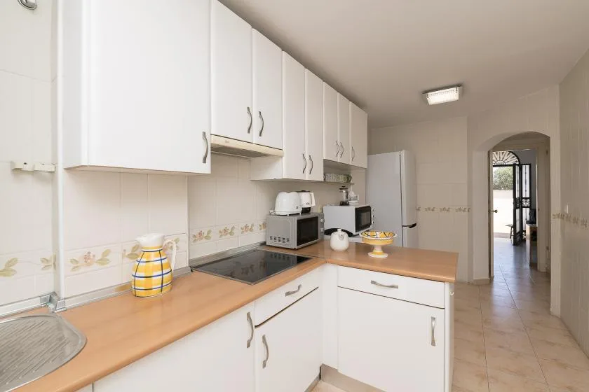 A bright kitchen with white cabinets, wood countertops, and a tiled floor.