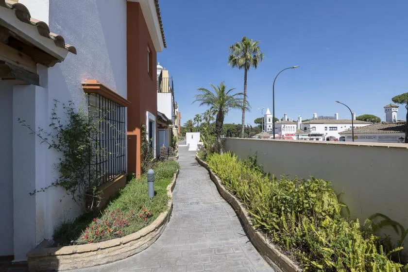 A paved walkway curves alongside a building and a hedge beneath a clear blue sky.