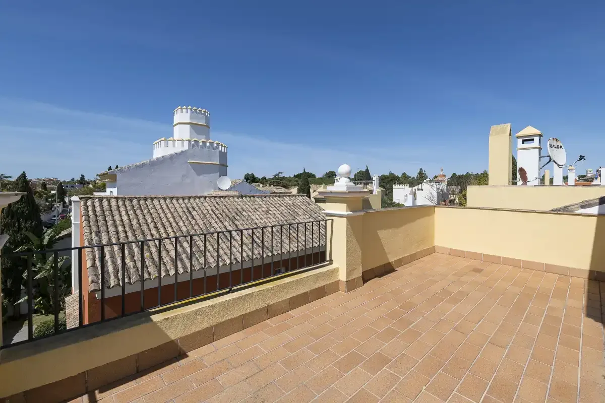 A sunny rooftop terrace overlooks nearby buildings beneath a clear blue sky.