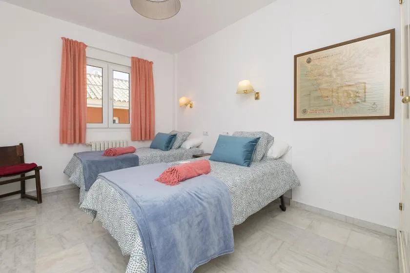 A bedroom with two beds, coral curtains, and framed artwork on the wall.