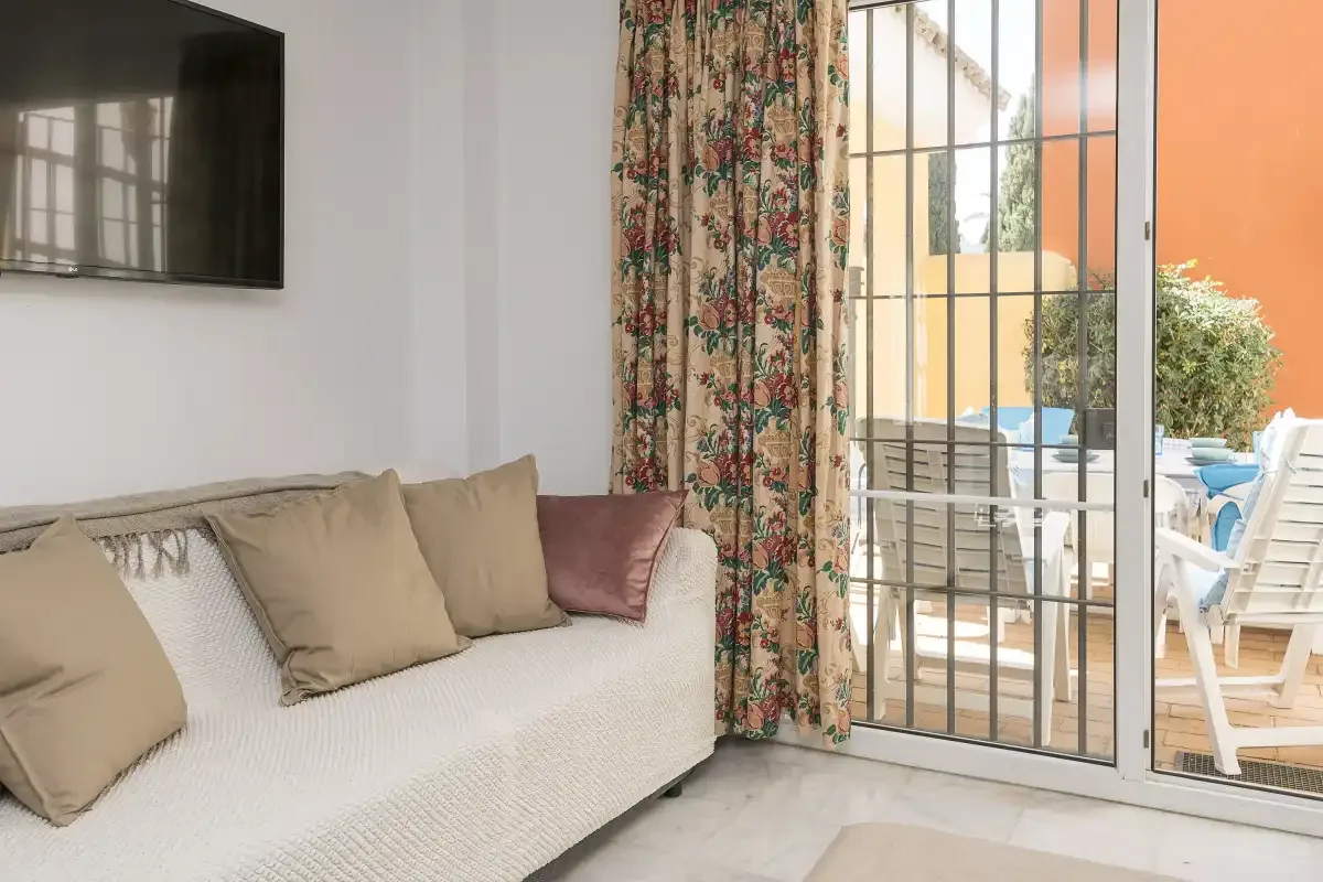 A living room with a light-colored sofa beside sliding glass doors opening onto a patio.
