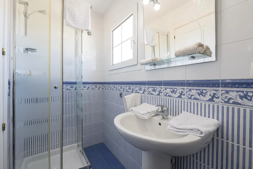 A tiled bathroom with a glass shower, sink, and wall mirror.