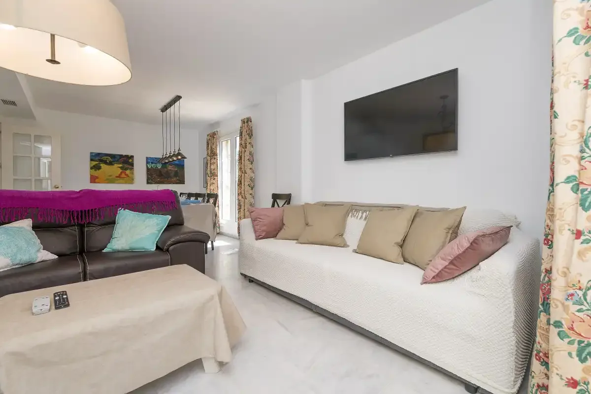 A bright living room with two seating areas and a wall-mounted television.