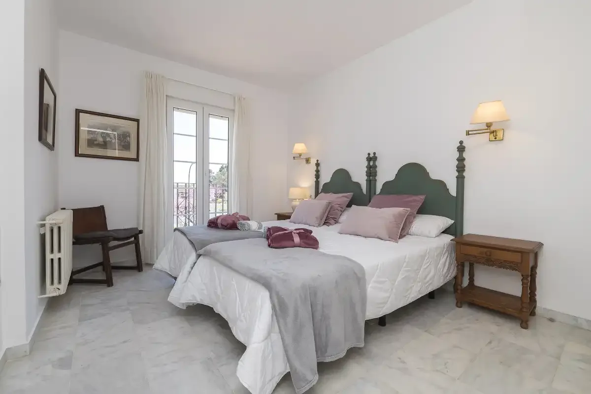 A bright bedroom with a double bed, bedside tables, and a window.