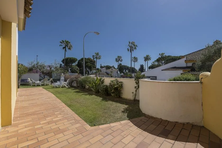 A paved outdoor patio borders a small grassy area and a low wall.