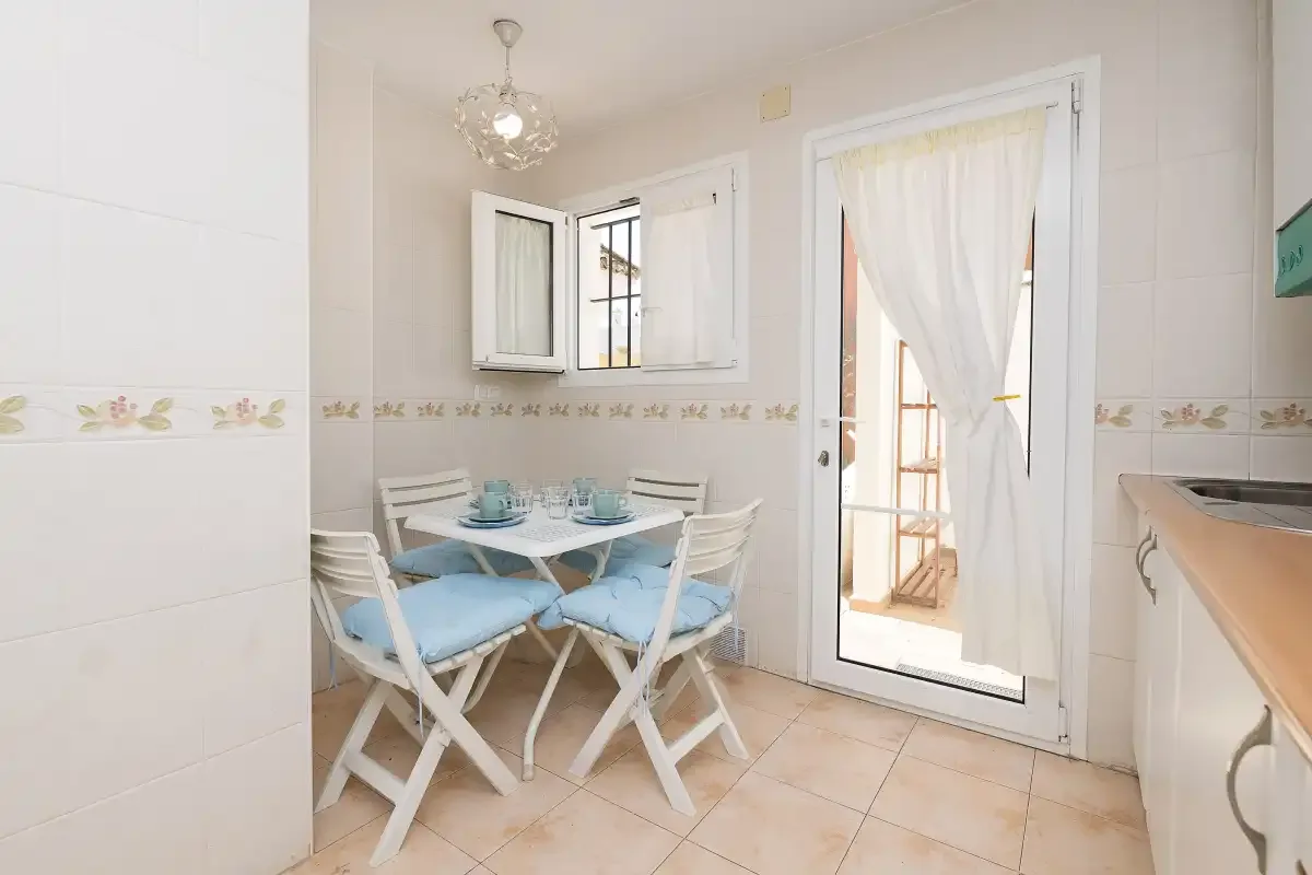 A bright dining area has a small table with blue seating beside a curtained glass door.