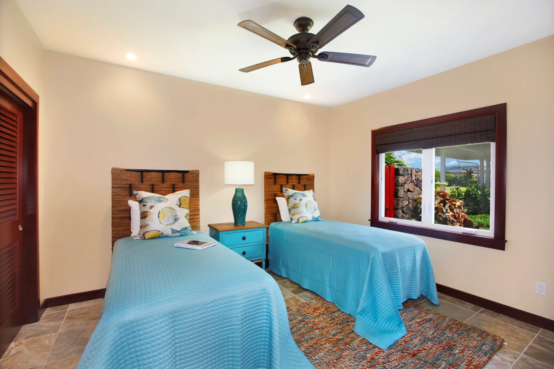 A bedroom with two beds covered in blue bedding and a window overlooking greenery.