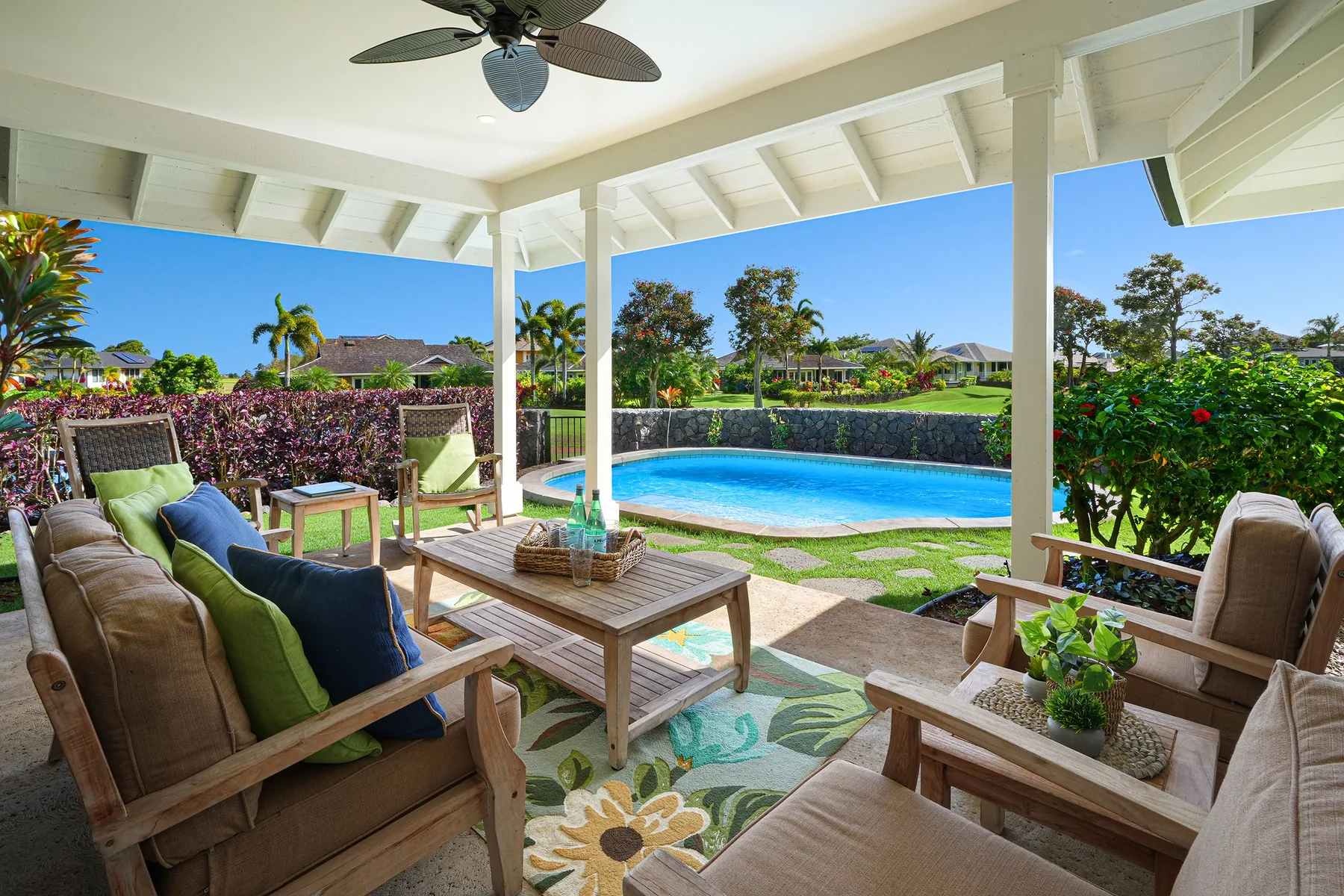 A covered patio with outdoor seating overlooks a swimming pool and garden.