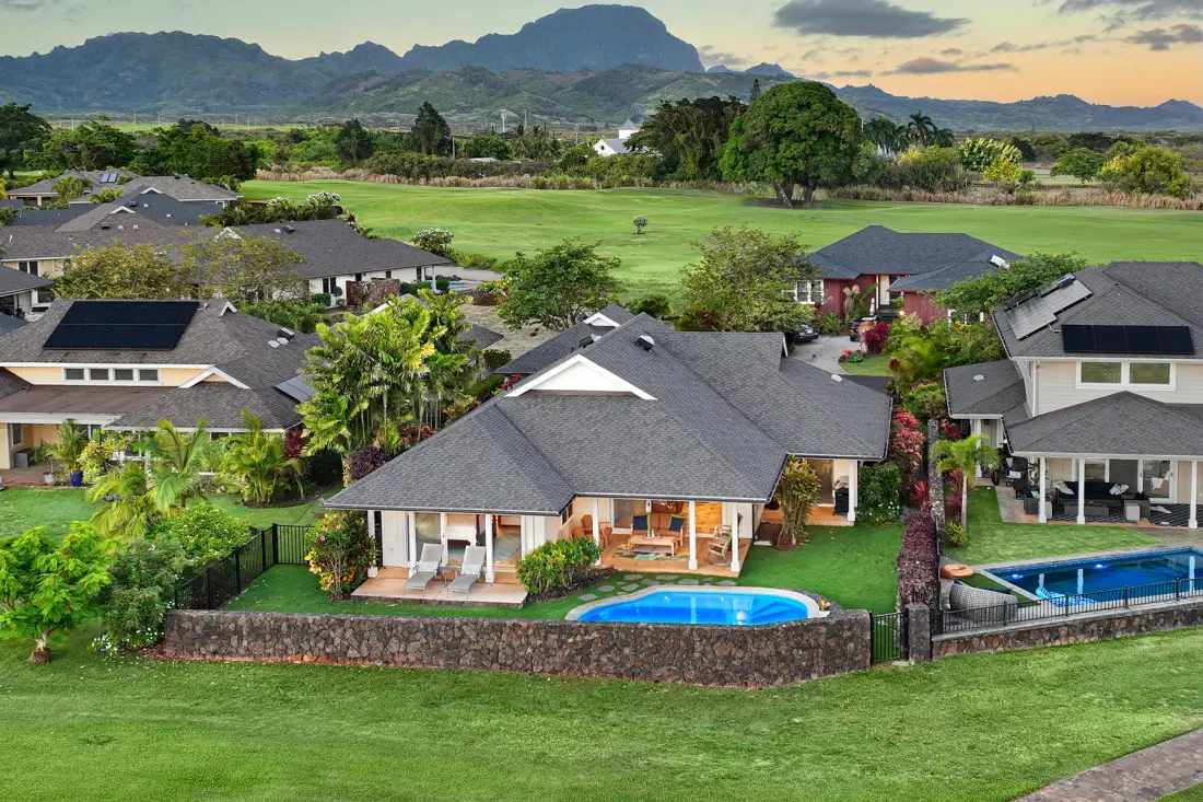 Vista aérea de casas con césped verde, una piscina y montañas a lo lejos.