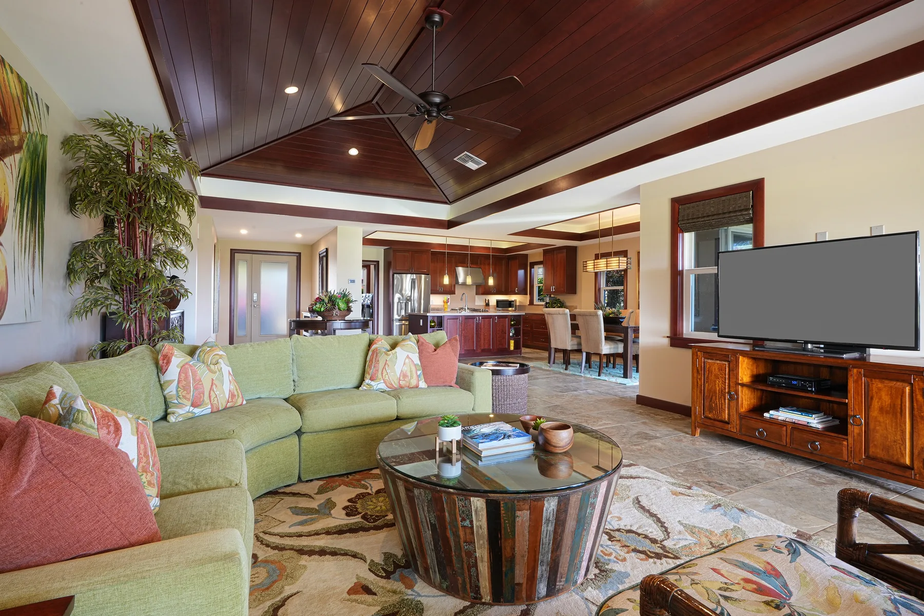 A spacious living room has green seating, a glass coffee table, and a television.