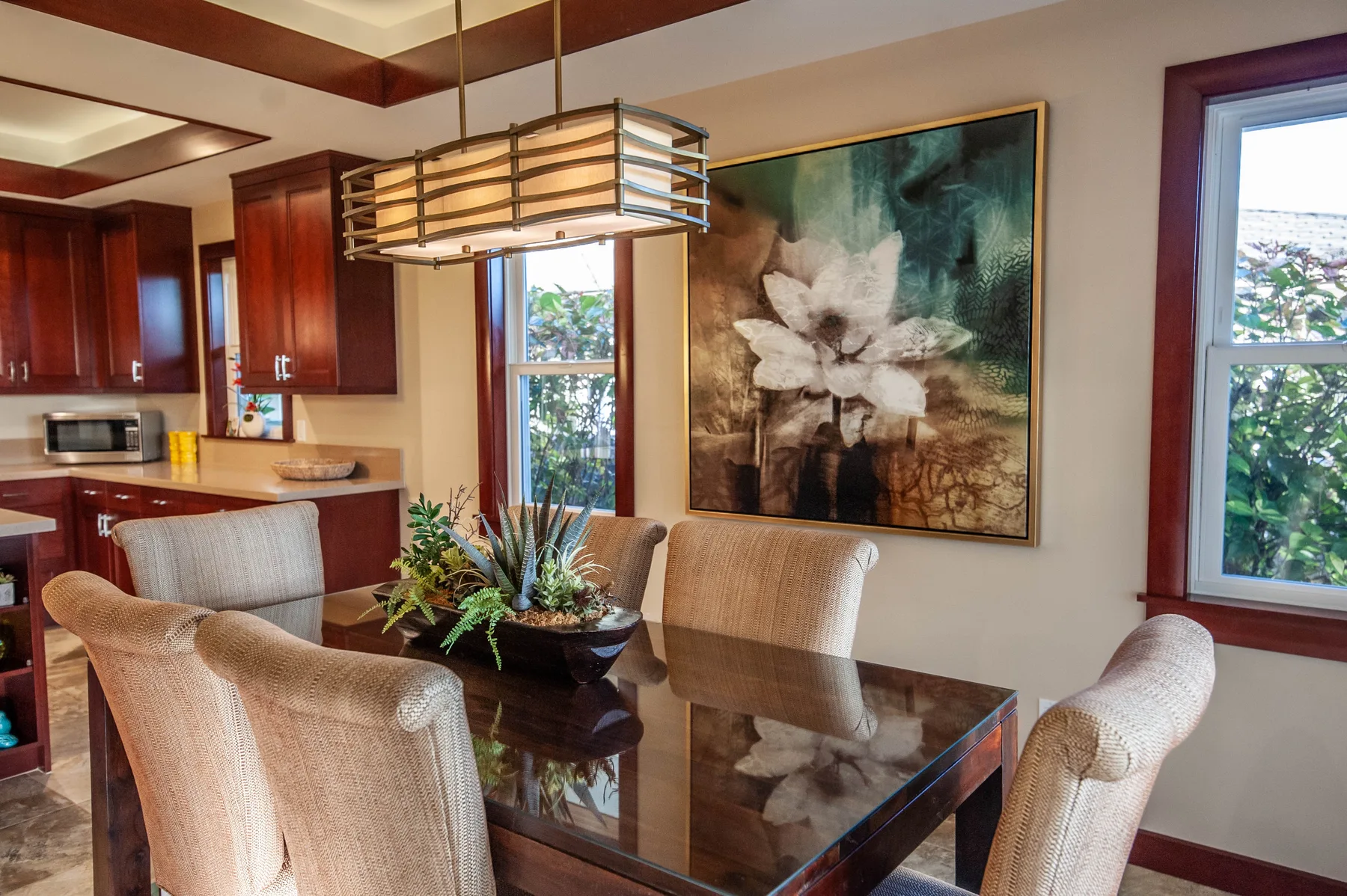 A dining area with a glass-top table, upholstered seating, and a large floral painting.