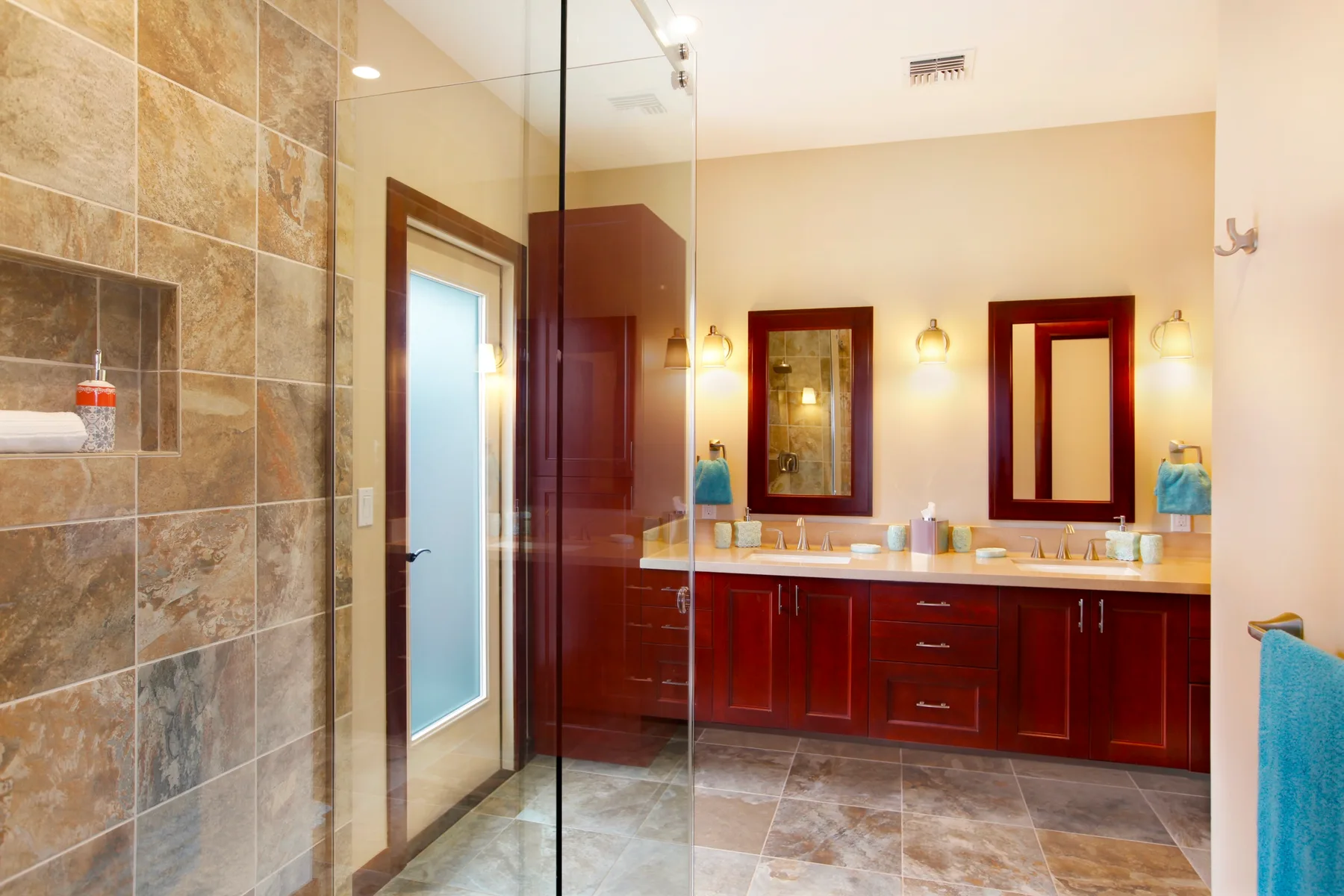 A bathroom with a glass shower beside a wooden vanity and mirrors.