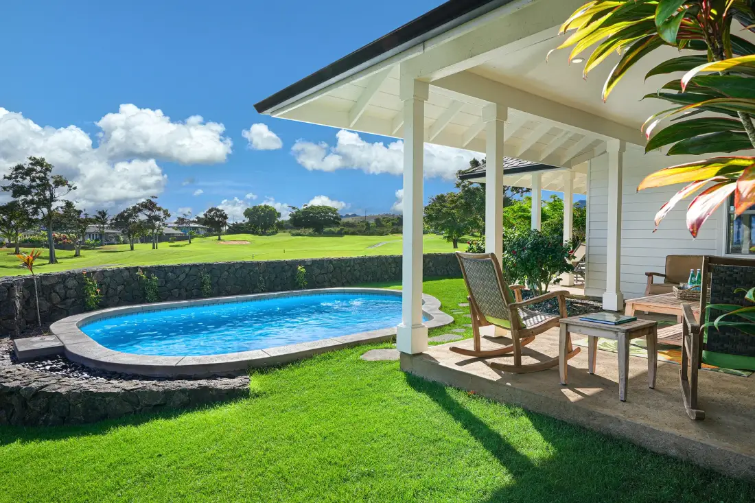A backyard patio overlooks a curved swimming pool and green lawn.