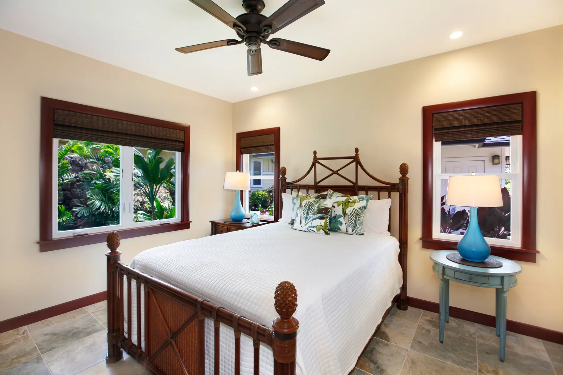 A bedroom with a wooden bed, white bedding, and windows overlooking greenery.