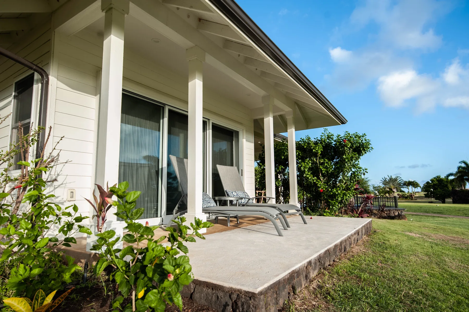 A covered patio with lounge seating overlooks a grassy outdoor area.