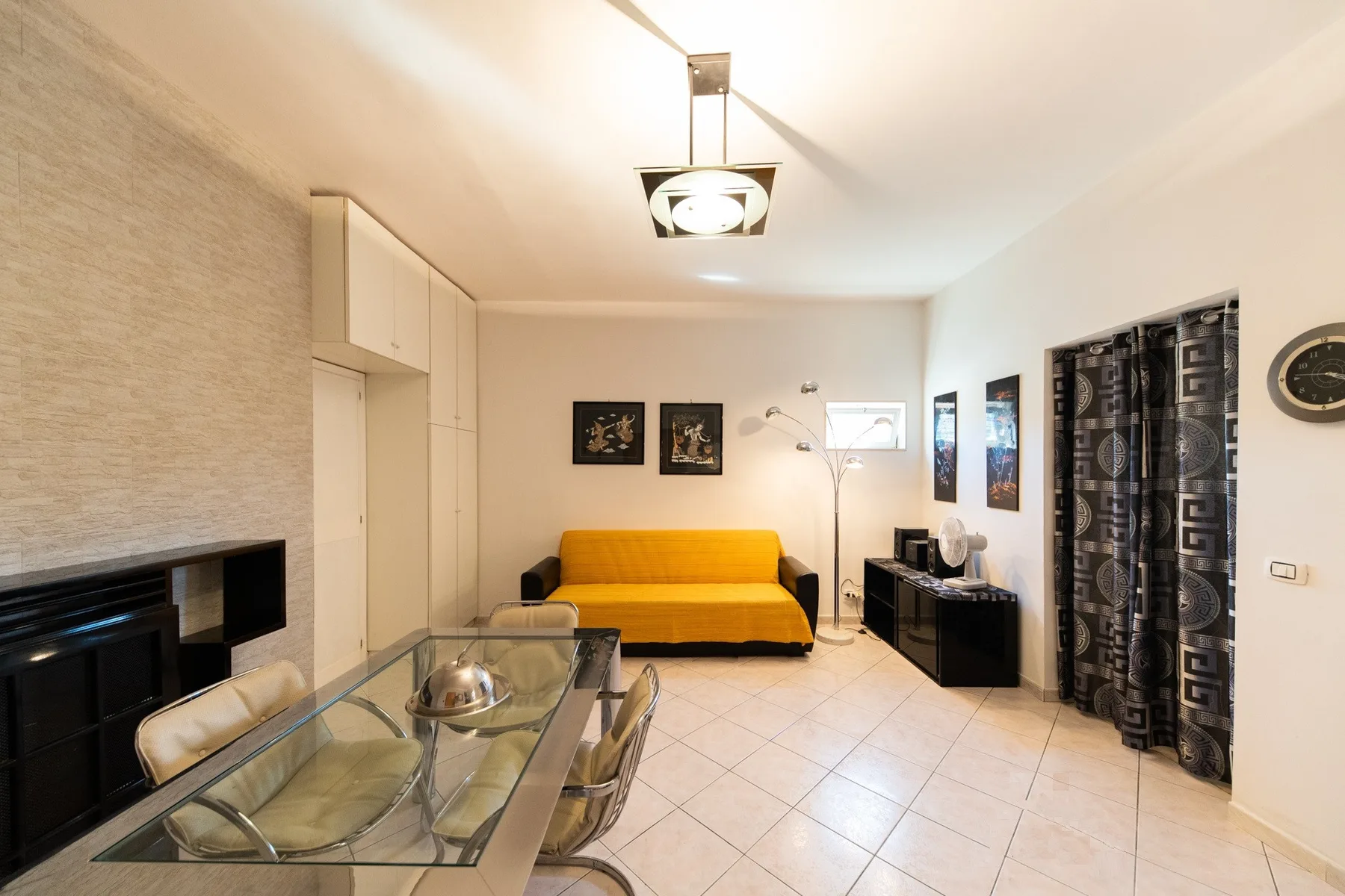 A living room with a yellow sofa and glass dining table.