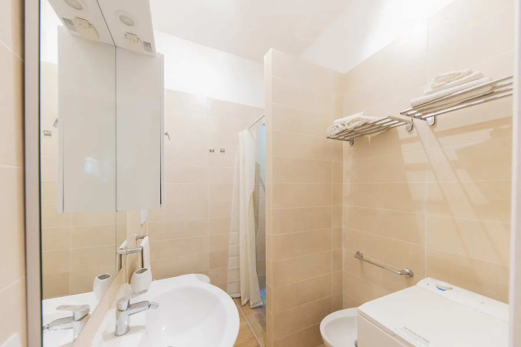 A tiled bathroom with a sink, shower, and towel racks.