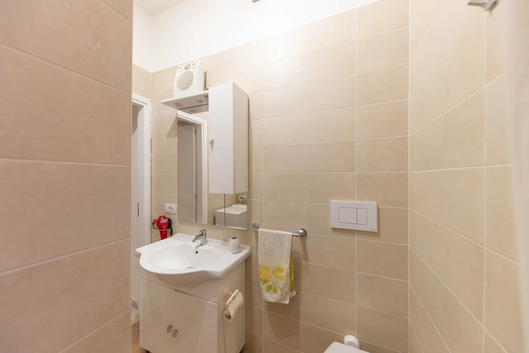A tiled bathroom with a sink, mirror, and towel.