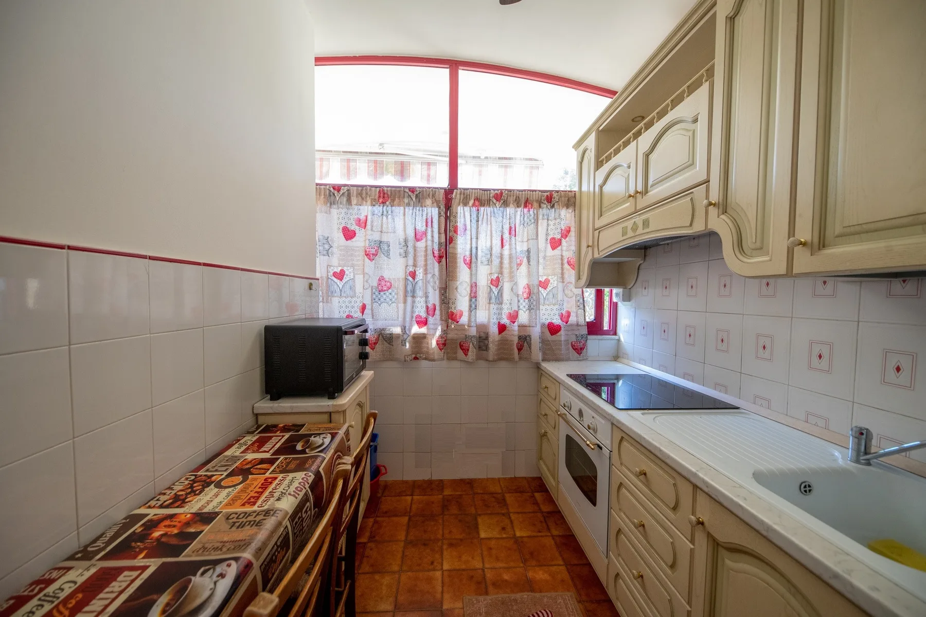 A tiled kitchen with patterned curtains above the counter and sink.