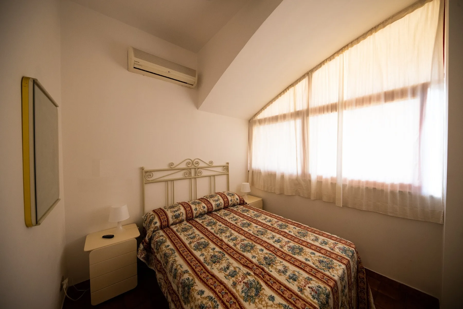 A bedroom with a patterned bedspread and a large curtained window.