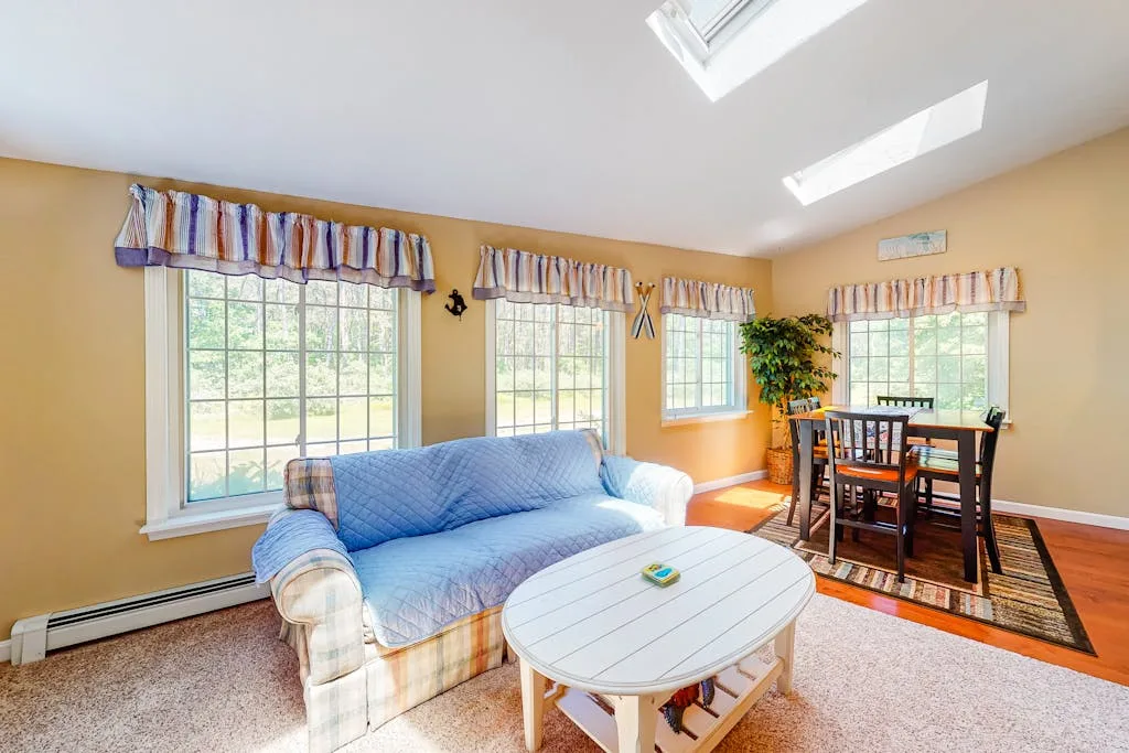 A bright living and dining area with seating, a table, and large windows.