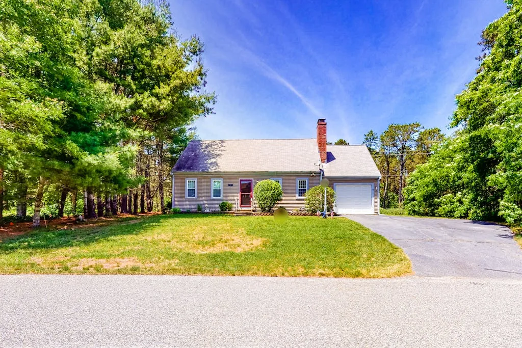 A detached house with a driveway sits among trees beneath a clear sky.
