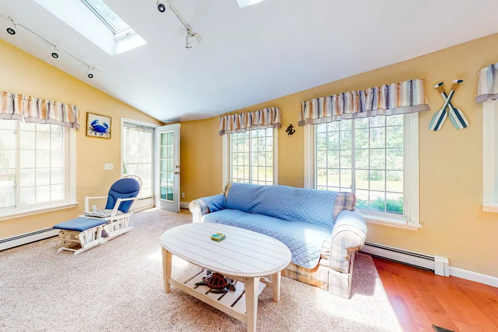 A bright sunroom has blue seating, large windows, and a white coffee table.