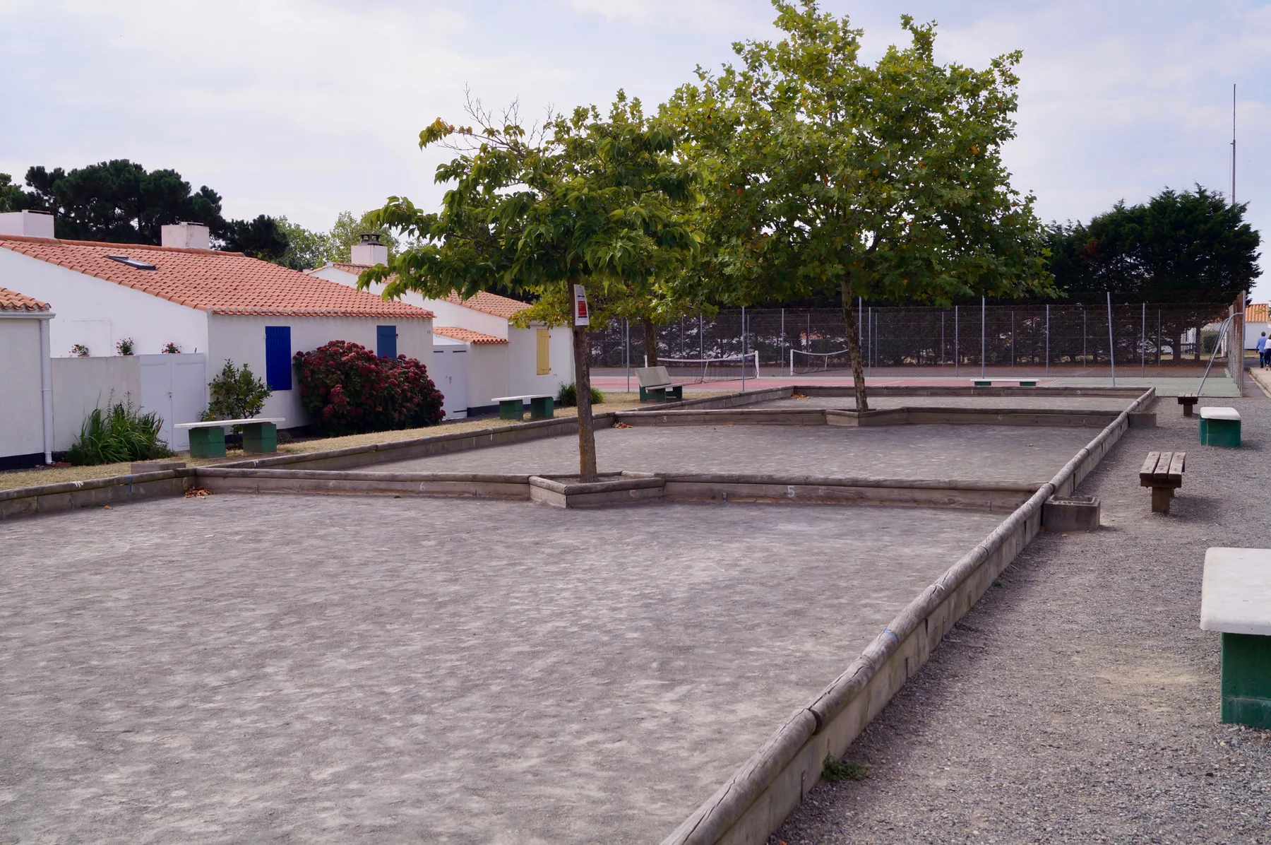 An outdoor paved recreation area has low raised borders, benches, and trees.