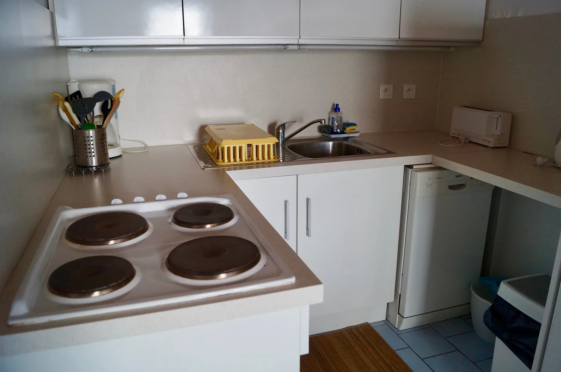 A compact kitchen with a stovetop, sink, and white cabinets.