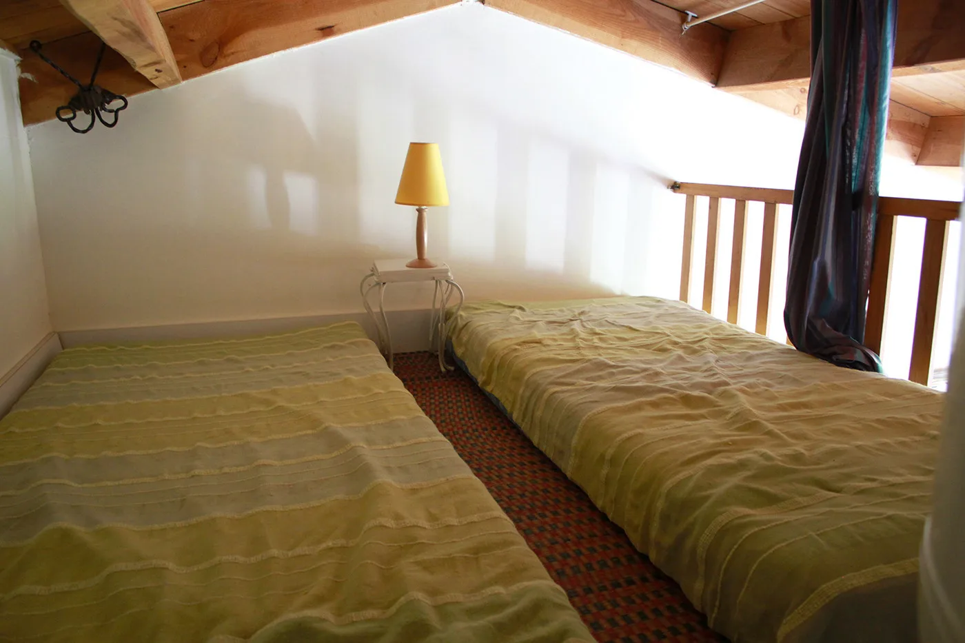 A bedroom with two beds and a small lamp beneath a sloped wooden ceiling.