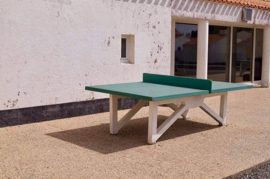 A green ping-pong table stands on a patio beside a building.