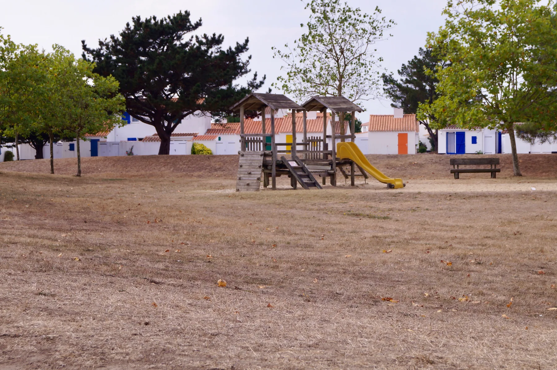A playground with a wooden play structure and slide stands in an open grassy area.