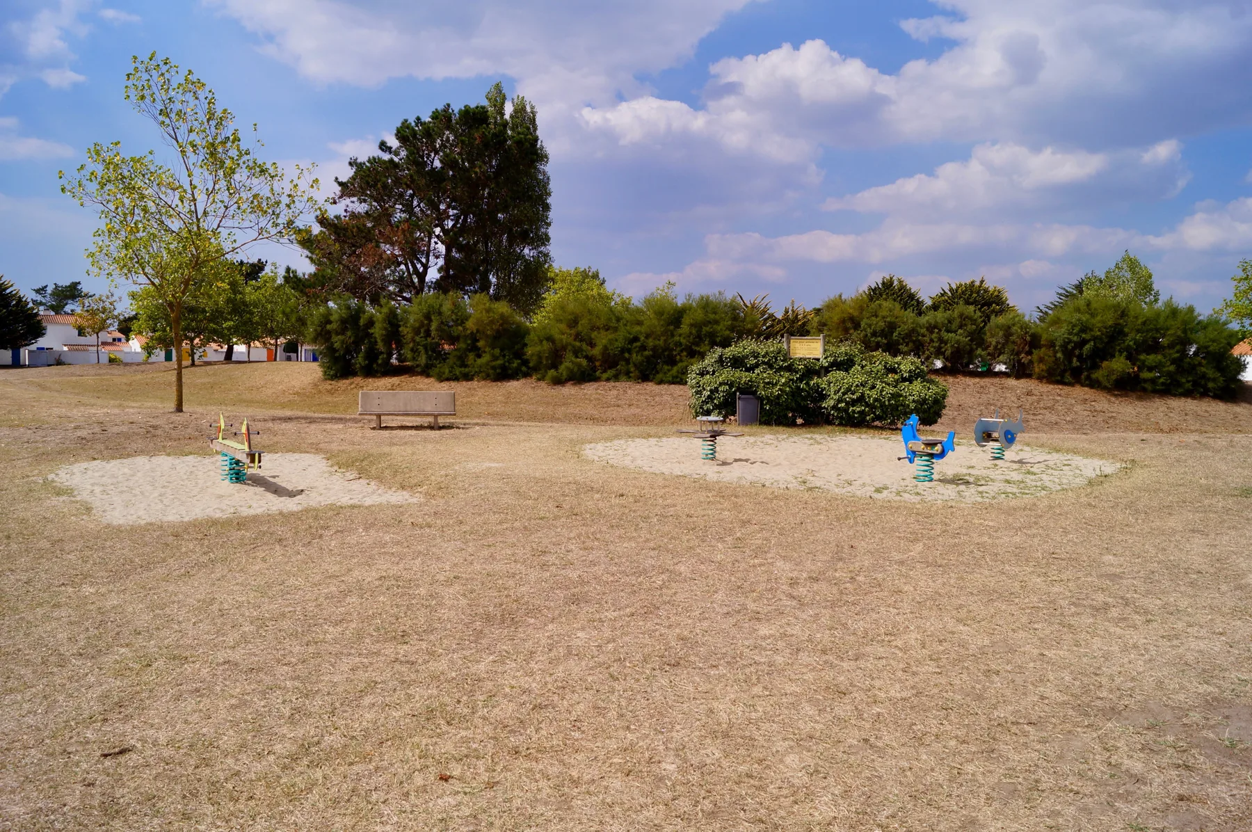 An open playground area with colorful play equipment and trees in the background.