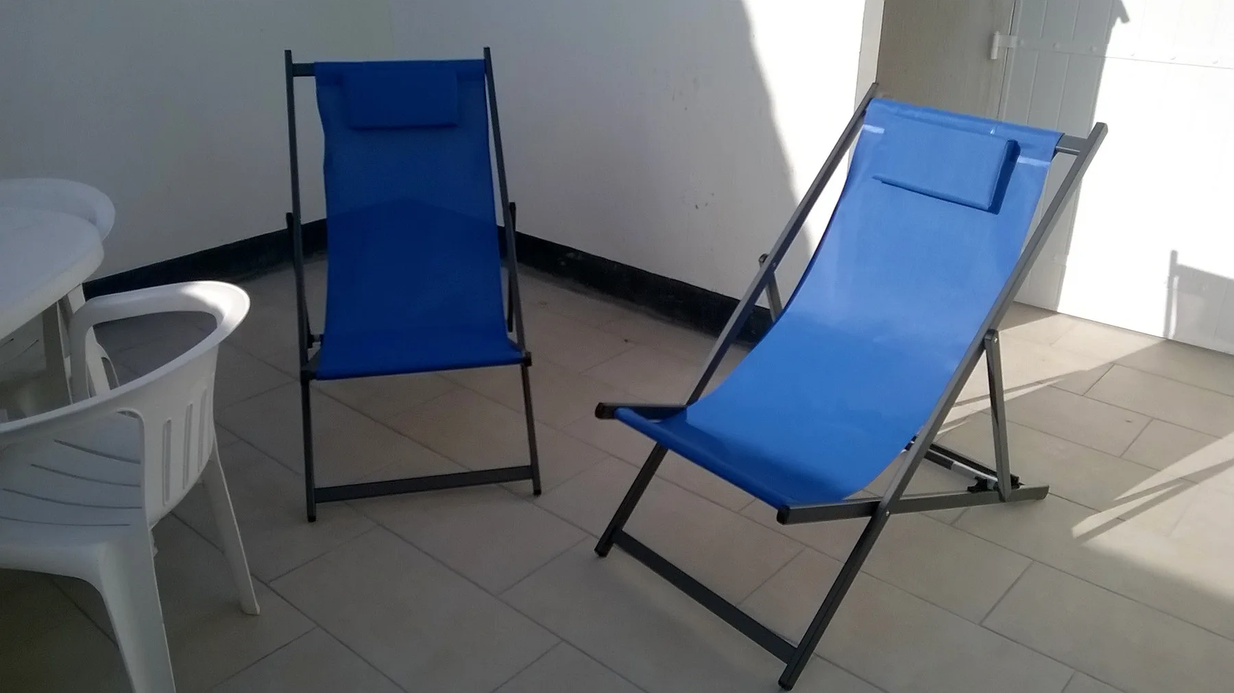 A tiled patio with blue reclining chairs and a small white table.