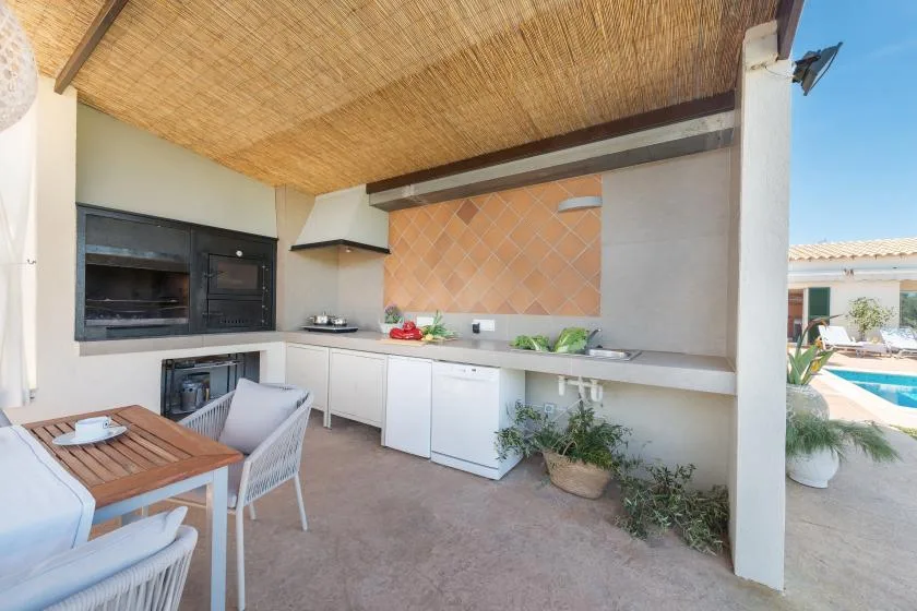 Una cocina exterior con una mesa de comedor bajo un techo de sombra trenzado.