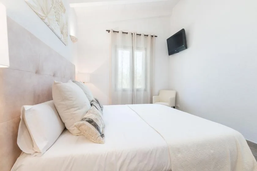 Un dormitorio luminoso con una cama bien hecha y un televisor en la pared.