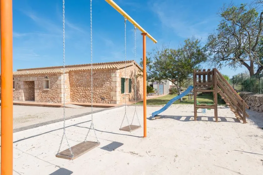 Una zona de juegos al aire libre con columpios y un tobogán de madera junto a un edificio de piedra.